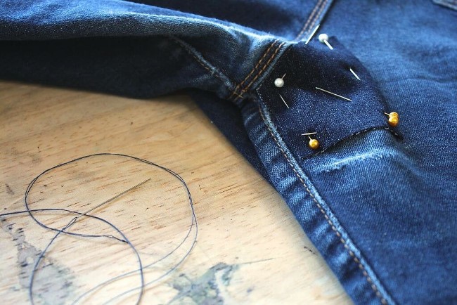 Вырежьте латку из старых джинс, приклейте с помощью клеевой ленты и прошейте ее по краям